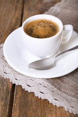 Cup of coffee with milk on sackcloth napkin on wooden