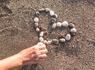 Woman's hand making heart of marine shingles on the sand.