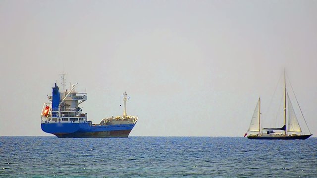Sailboat is passing near transportation tanker boat