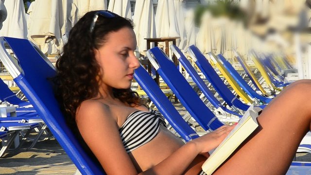teenager girl reading a book on a beach