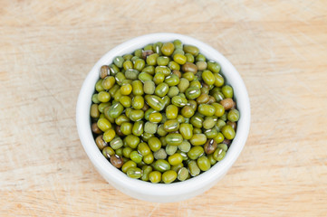 Green mung beans in white ceramic bowl on wood background.