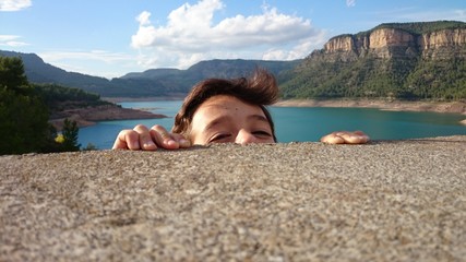 Niño asomándose por pared con embalse al fondo