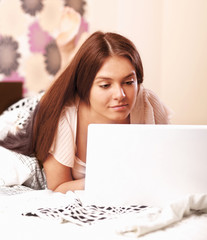 Young woman lying on the bed with laptop