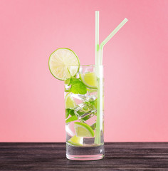 Glass of mojito cocktail on pastel pink background