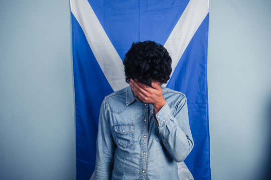 Depressed man standing in front of scottish flag