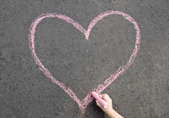 child hand drawing heart on the street