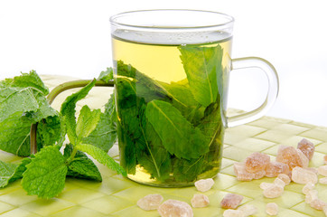 Cup of mint tea with brown cane sugar and fresh mint on a green
