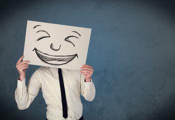 Businessman holding a paper with smiley face in front of his hea