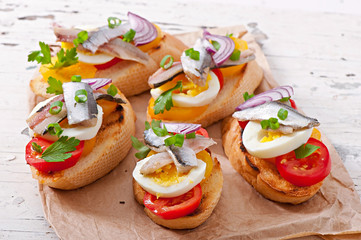Crostini with anchovies, tomatoes and egg, decorated with greens