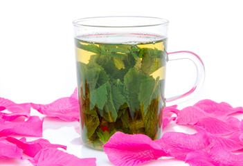 Cup of mint tea surrounded with pink petals