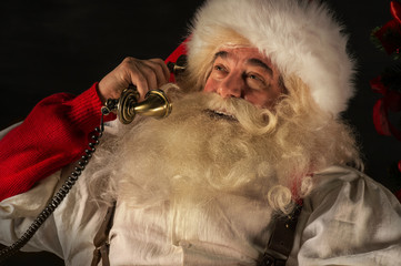 Portrait of emotional Santa Claus calling phone at home