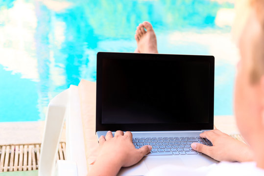 barefoot male turn on the computer sitting by the pool