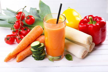 Glass of fresh carrot juice and vegetables on wooden table