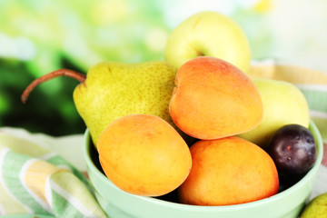 Ripe fruits in bowl on table on bright background