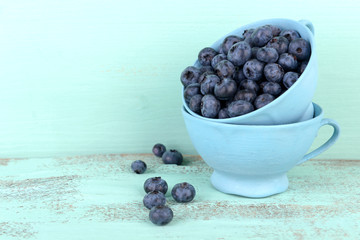 Tasty ripe blueberries in cups, on wooden table