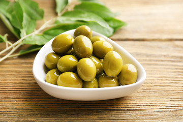 Green olives in bowl with leaves on table close-up