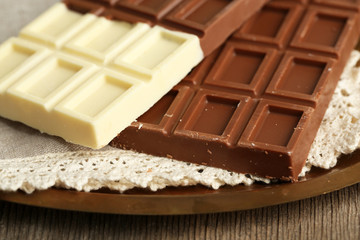 Chocolate bars on napkin, on tray, on wooden background