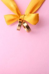 Wedding rings tied with ribbon on color background