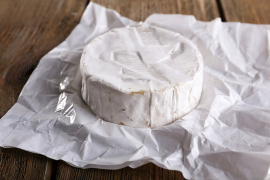 Camembert cheese on paper on wooden background