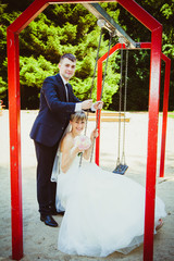 beautiful young wedding couple in park, blonde bride on swing an
