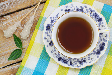 Black tea in vintage cup, sugar sticks on colorful cloth on wood