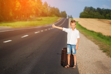 Smiling child with suitcase traveling hitchhiking. summer road