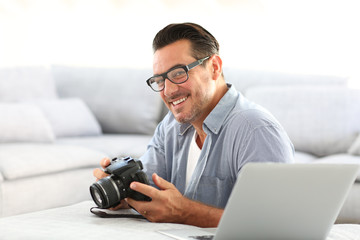 Man at home using reflex camera and laptop