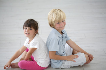 Brother and sister sitting back to back on the floor