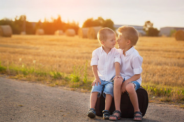 two brothers sit on a suitcase on the road in the summer at suns