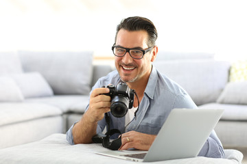 Man at home using reflex camera and laptop
