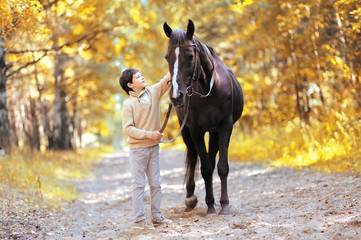 Autumn season happy teenager boy and horse walking in forest