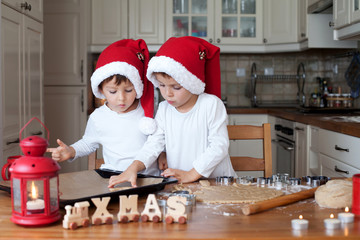 Two cute boys with santa hat, preparing cookies in the kitchen