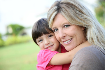 Cheerful woman embracing little girl in arms