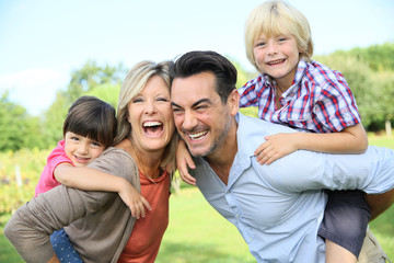 Parents giving piggyback ride to kids in park - obrazy, fototapety, plakaty