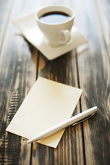 Note, paper, pen and cup of coffee on a wooden table