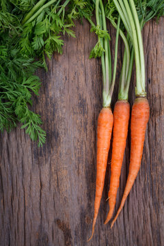 Bunch of fresh carrots with green leaves over wooden background