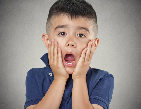 Child with astonished face expression on grey wall background 