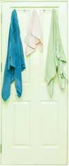Blue, Pink and Green towel hang on a wooden door.