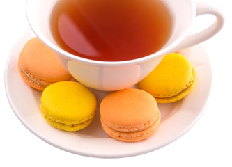 A cup of tea and yellow and orange colored macarons 