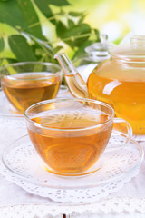 Teapot and cups of tea on table on bright background