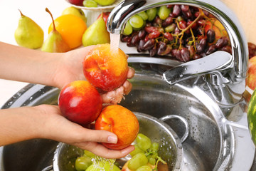 Woman's hands washing peaches and other fruits in colander in