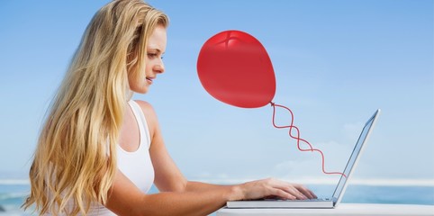 Composite image of pretty blonde using her laptop at the beach