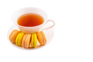 A cup of tea and yellow and orange colored macarons 