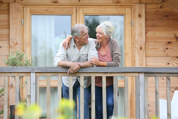 Senior couple standing oustide log cabin in countryside