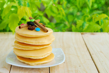 Stack of pancakes and syrup in plate on wooden table with green