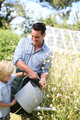 Father and son watering plants in garden