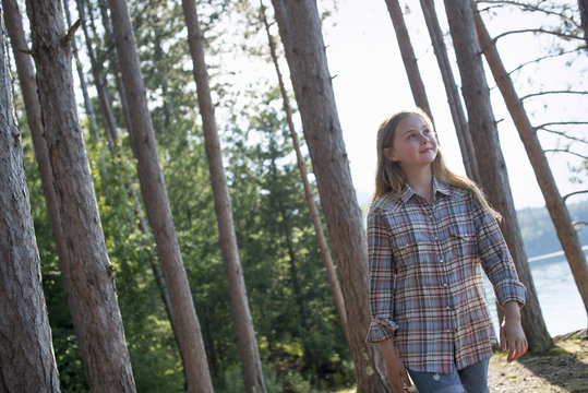 A girl walking in woodland beside a lake in summer.