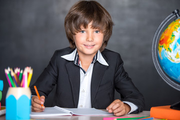 Cheerful school boy writing in notebook