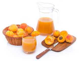 Glass and jug of apricot juice with a basket of apricots and sli