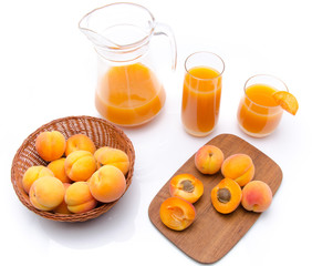 Jug and glasses of apricot juice with whole and sliced ripe apri